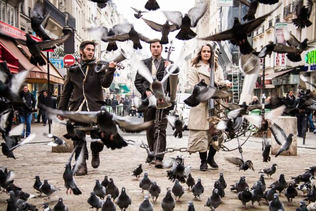 trois musiciens dans la rue avec des dizaines de pigeons
